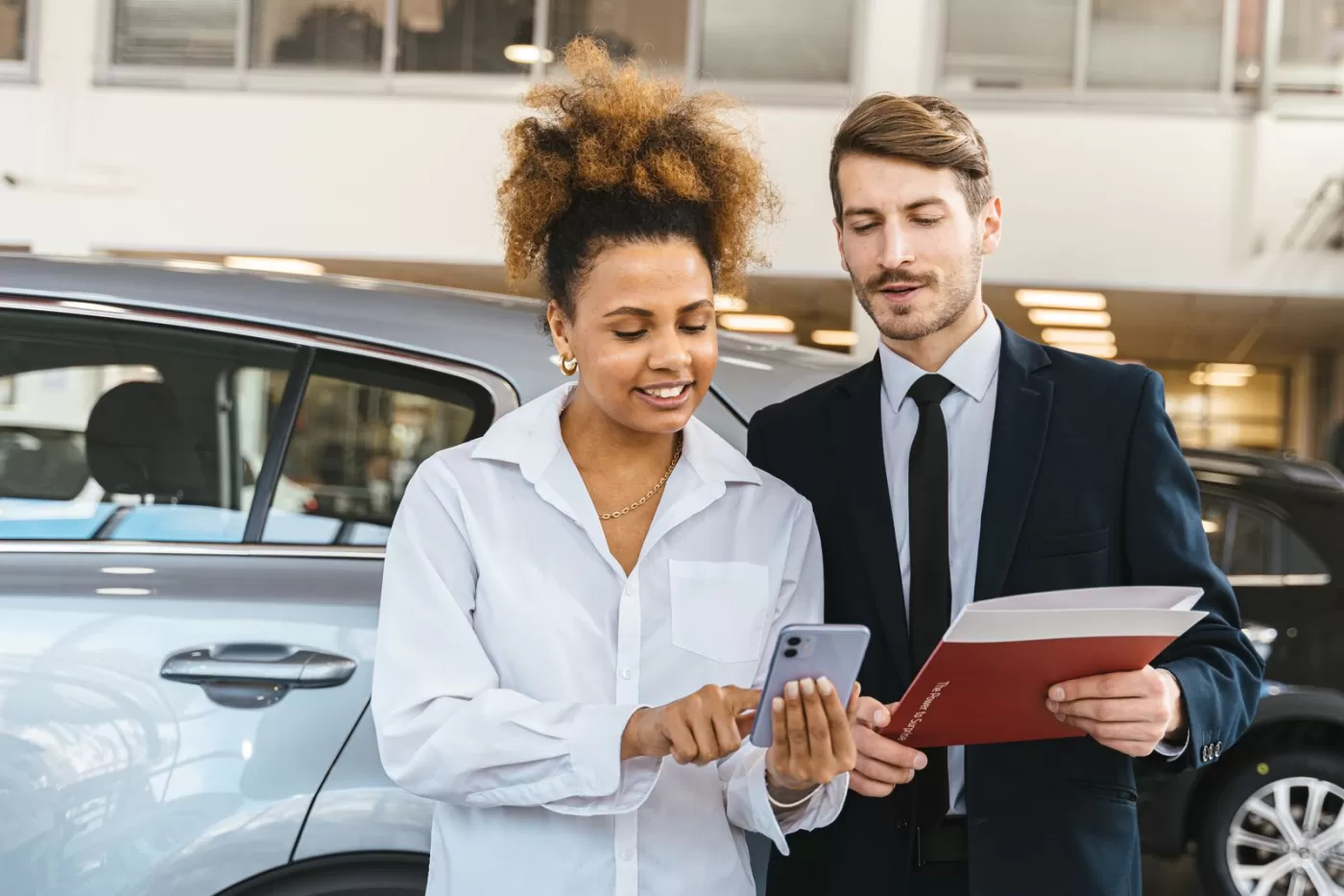A customer and a salesperson looking at a text conversation on a phone beside a vehicle