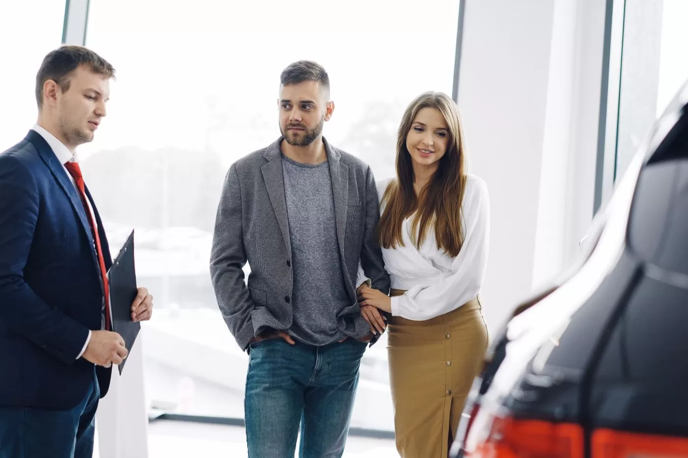 A salesperson greeting a couple beside a new vehicle on the showroom floor