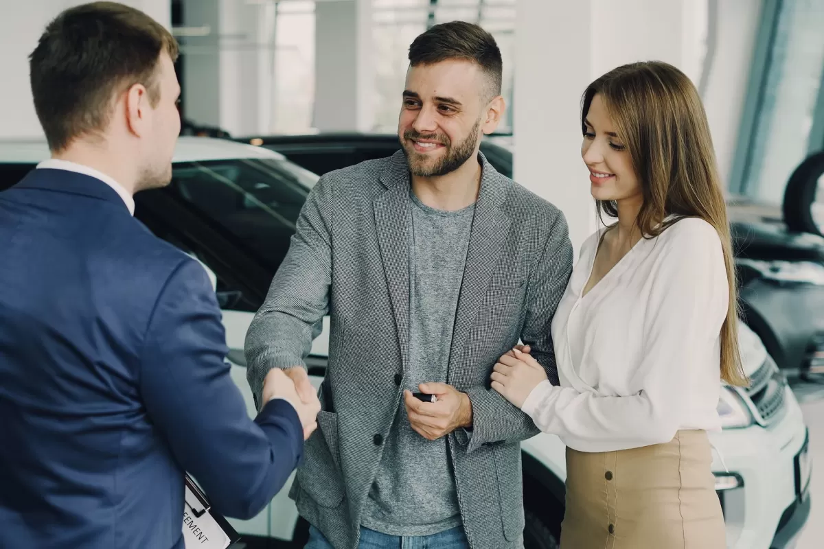 A salesperson shaking hands with a happy couple after a vehicle purchase