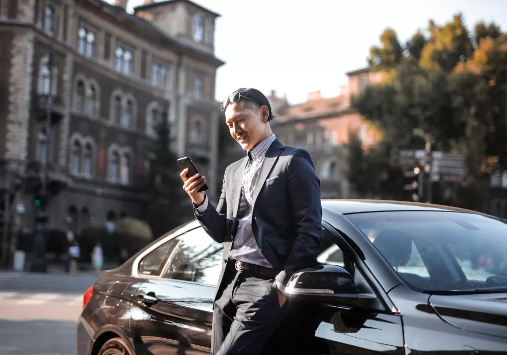 A smiling salesperson answering a new lead on his phone beside a vehicle